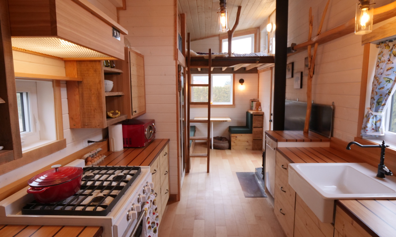 Shown is the interior of a tiny house, showing the kitchen in the foreground with lots of wood everywhere.