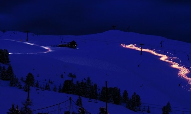 People with torches at night, going down a snowy mountain.