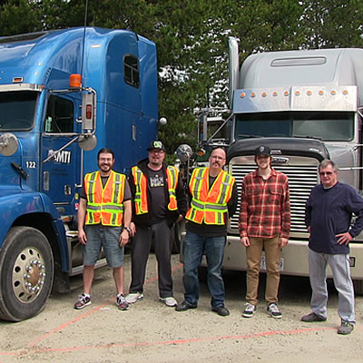 Picture of group of people standing in front of semi-trucks. 