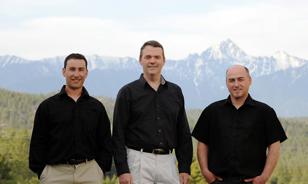 Three men in black shirts standing together with the mountains in the background.