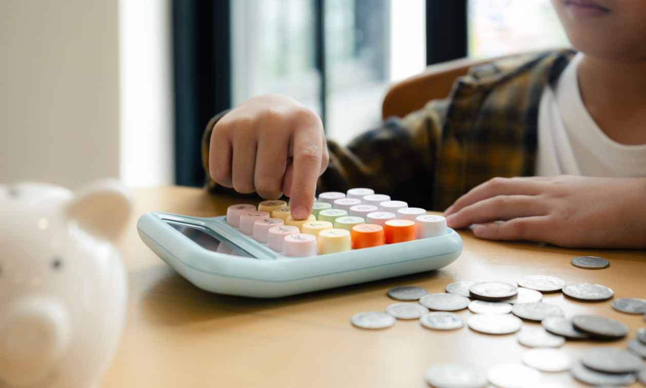 Person using a calculator with coins and a piggy bank on the side
