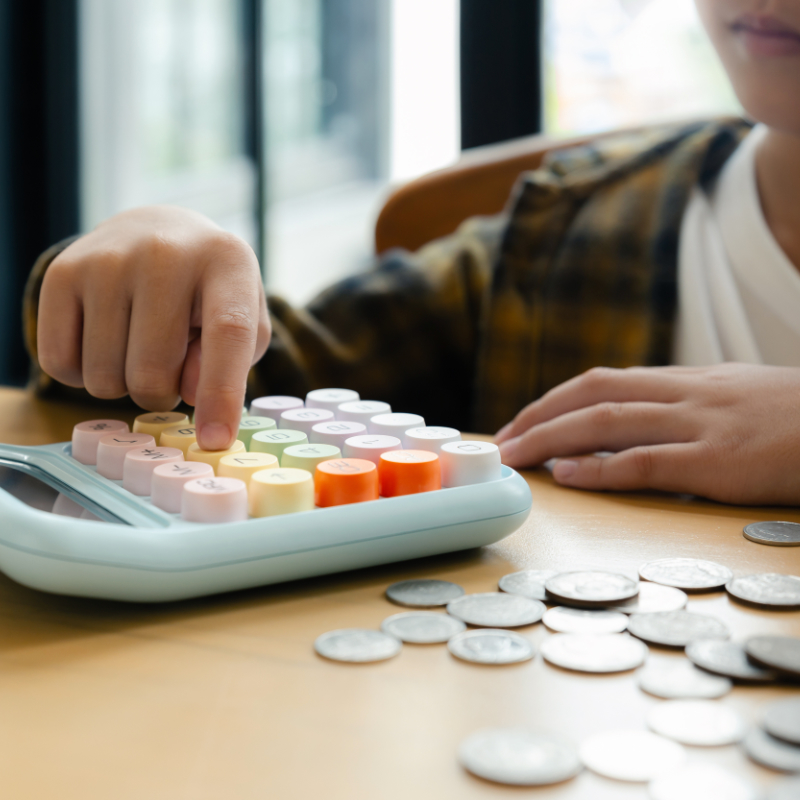 Person using a calculator with coins and a piggy bank on the side
