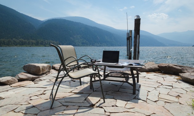 Two chairs and a desk with a computer on it, overlooking a lakeside view

