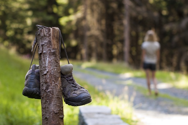 A woman is walking away barefoot after she left her biking boots hanging from a wooden post.