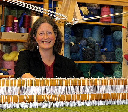 lady sitting at a wooden loom smiling
