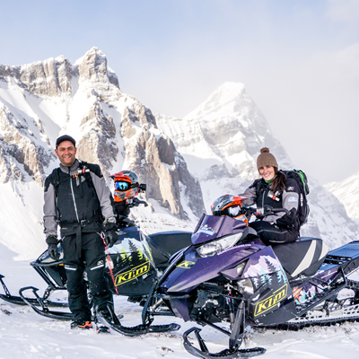 A young man and woman on snowmobiles in the mountains. 