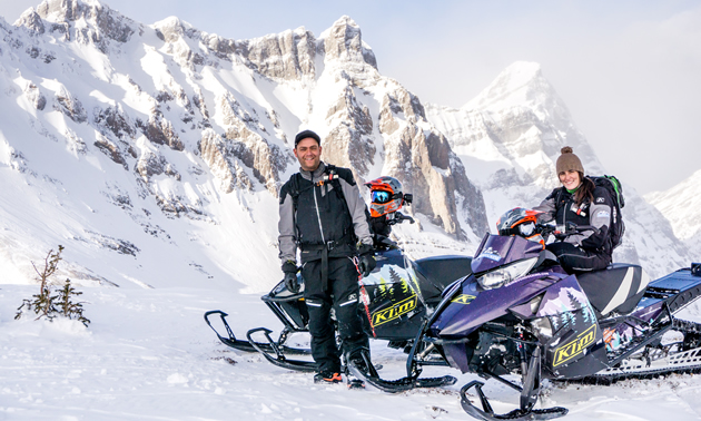 A young man and woman on snowmobiles in the mountains. 