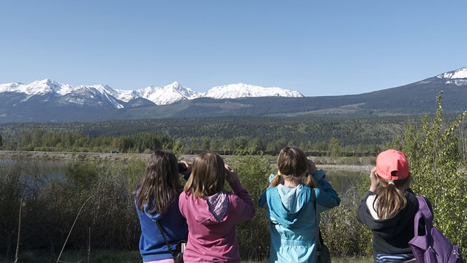 A picture of a group of kids, backs turned towards the viewer, looking at a scenic expanse of mountains in the distance. 