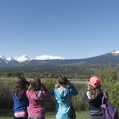 A picture of a group of kids, backs turned towards the viewer, looking at a scenic expanse of mountains in the distance. 