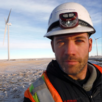 Randolph Seibold wears a hard hat and headlamp. He's standing next to a wind tower in a snowy landscape.